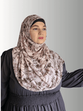 A woman wears a blush pink chiffon hijab adorned with brown floral patterns.