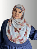 A woman wears a flowy chiffon hijab with pink and red floral patterns on a muted blue-gray background.