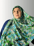 Woman wearing a green and blue floral chiffon hijab, draped elegantly over her shoulders.