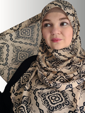 woman wearing the Sandstone Elegance Chiffon Hijab, a beige chiffon hijab with black geometric patterns. The hijab drapes beautifully, adding a sophisticated touch to her modest look.