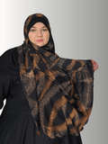 A woman wearing the Luxe Noir Essence Veil, featuring a black chiffon overlay with deep, rich brown patterns. The hijab has a soft jersey base for full coverage and a comfortable, non-slip fit. The intricate design and earthy tones create a sophisticated and elegant look.
