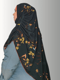 A black chiffon hijab with golden floral patterns and rust-colored stitching along the edges, styled with an orange base. Front and back views highlight its flowing drape and full coverage design."
