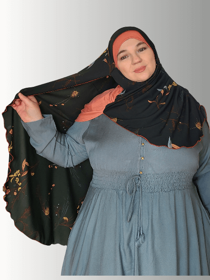 A black chiffon hijab with golden floral patterns and rust-colored stitching along the edges, styled with an orange base. Front and back views highlight its flowing drape and full coverage design.