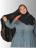A black chiffon hijab with golden floral patterns and rust-colored stitching along the edges, styled with an orange base. Front and back views highlight its flowing drape and full coverage design."
