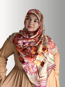 A woman wears a 48x48" silk-blend square hijab with a rich floral design in warm autumn hues.
