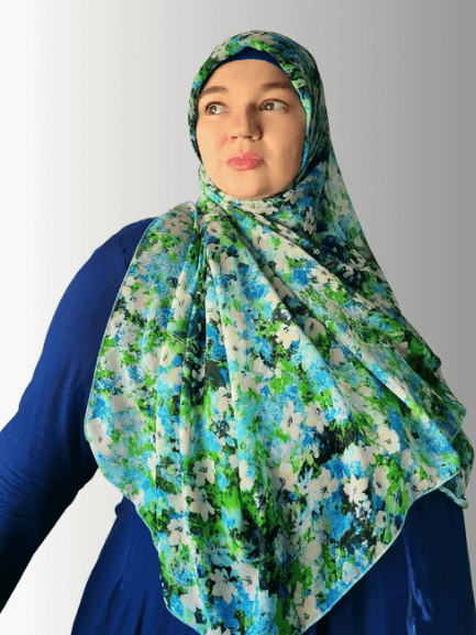 Woman wearing a blue and green floral chiffon hijab, gently holding the fabric to showcase its airy texture.