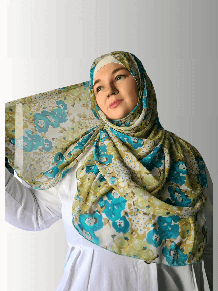 Woman wearing a blue and green floral chiffon hijab, gently holding the fabric to showcase its airy texture.
