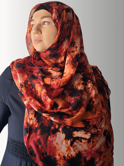 Woman wearing a red and black abstract chiffon hijab, looking to the side with a confident expression.