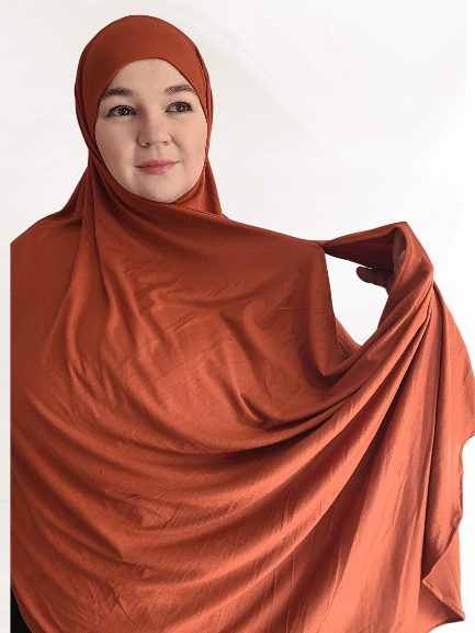 Warm terracotta-toned double loop instant hijab with attached undercap, styled in soft drapes showing earthy elegance and midweight jersey texture.
