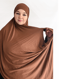 A rich, chestnut-toned brown jersey hijab in a double loop style with attached undercap, displayed in soft natural lighting.
