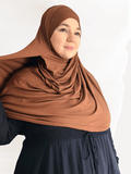 A rich, chestnut-toned brown jersey hijab in a double loop style with attached undercap, displayed in soft natural lighting.
