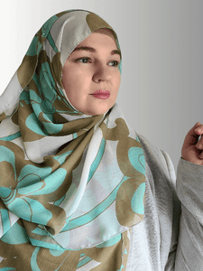 A woman wears a chiffon hijab with large teal and beige swirl patterns, styled loosely.