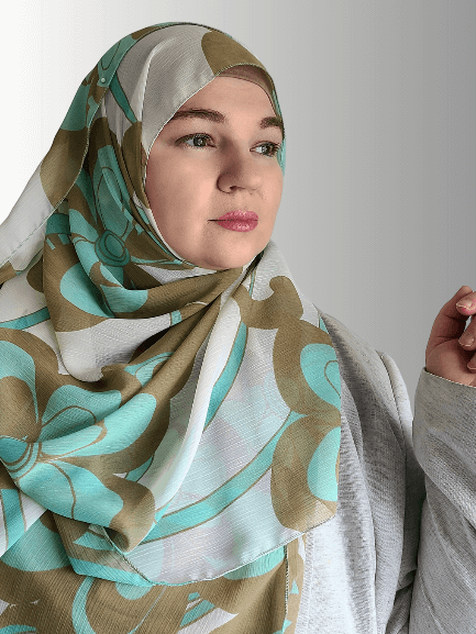 A woman wears a chiffon hijab with large teal and beige swirl patterns, styled loosely.
