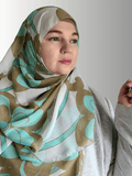 A woman wears a chiffon hijab with large teal and beige swirl patterns, styled loosely.