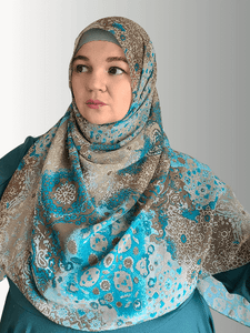 A woman wears a chiffon hijab with an intricate blue and brown mosaic design, styled gracefully.
