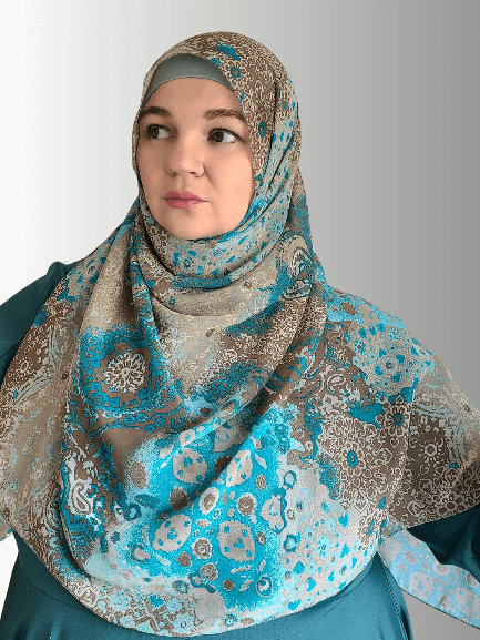  A woman wears a chiffon hijab with an intricate blue and brown mosaic design, styled gracefully.