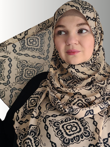woman wearing the Sandstone Elegance Chiffon Hijab, a beige chiffon hijab with black geometric patterns. The hijab drapes beautifully, adding a sophisticated touch to her modest look.