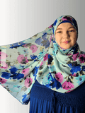 Woman wearing a sky-blue chiffon hijab with blue, magenta, and black floral patterns, holding the fabric to showcase its softness and flow.